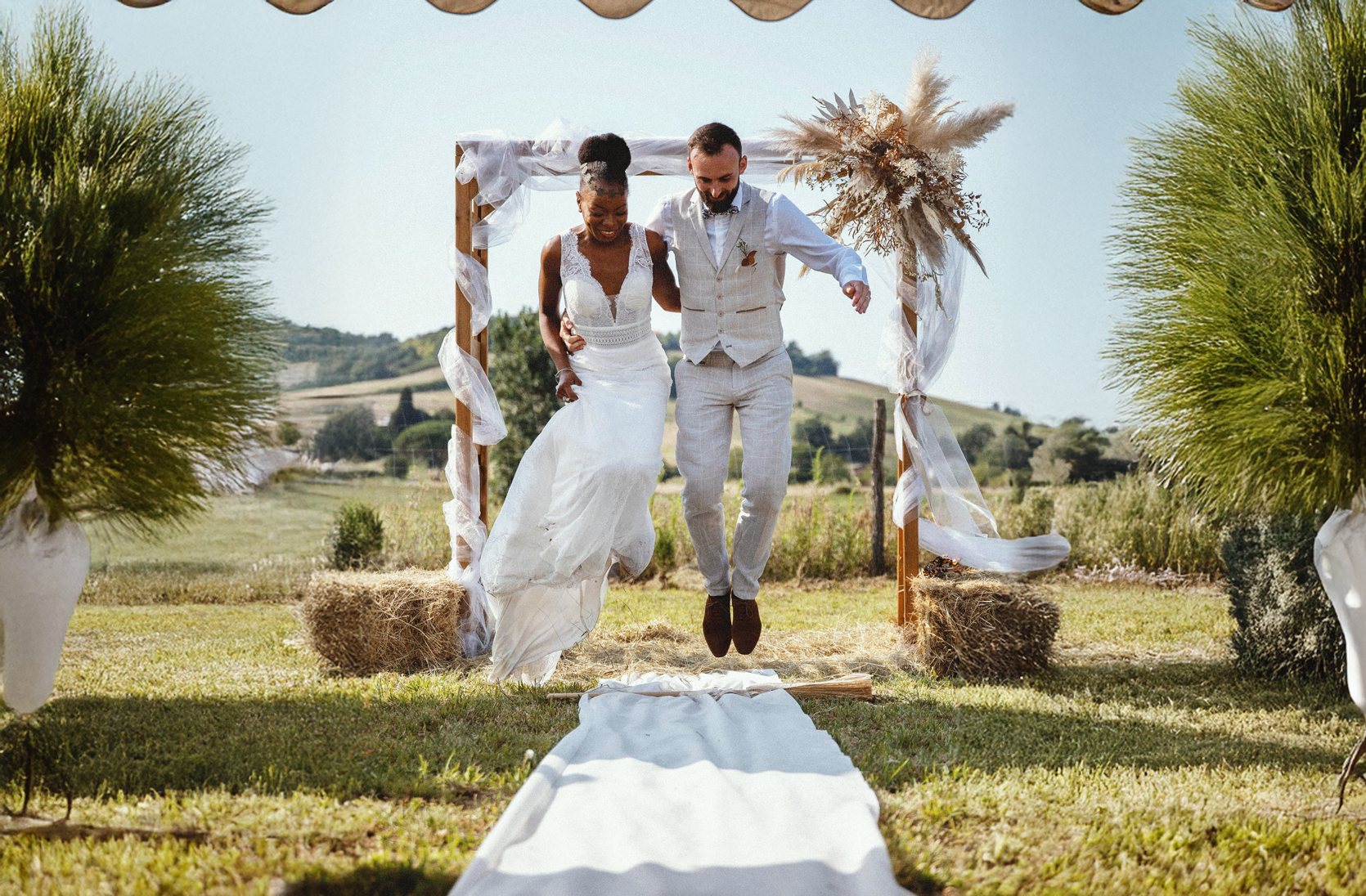 Mariés sautant de joie sous une arche fleurie, mariage à la campagne dans le Tarn